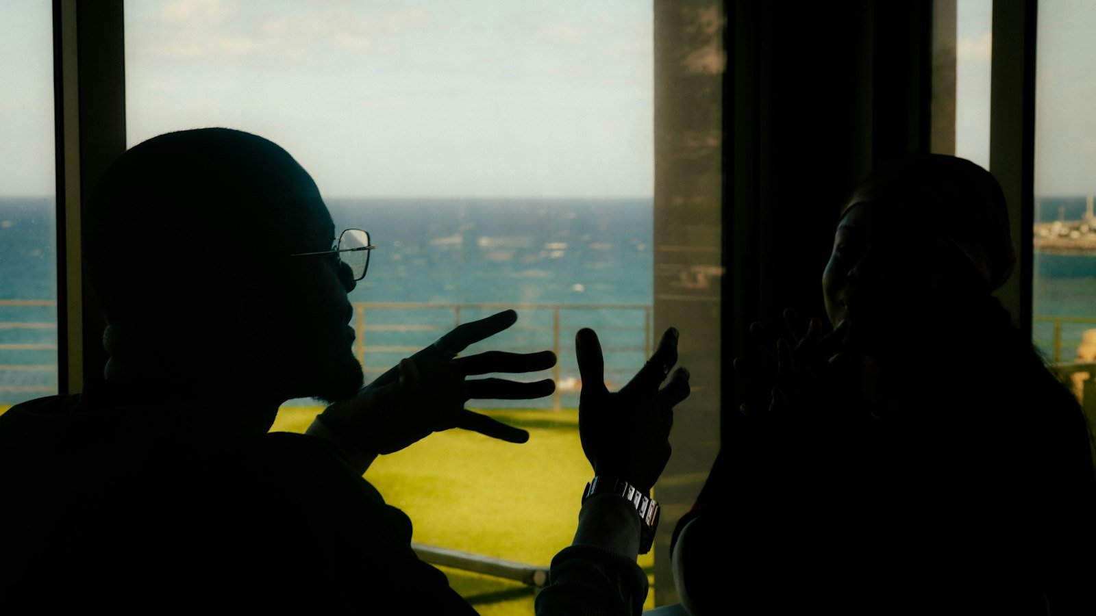 Business opportunity seekers: Two people silhouetted talking by a window overlooking ocean