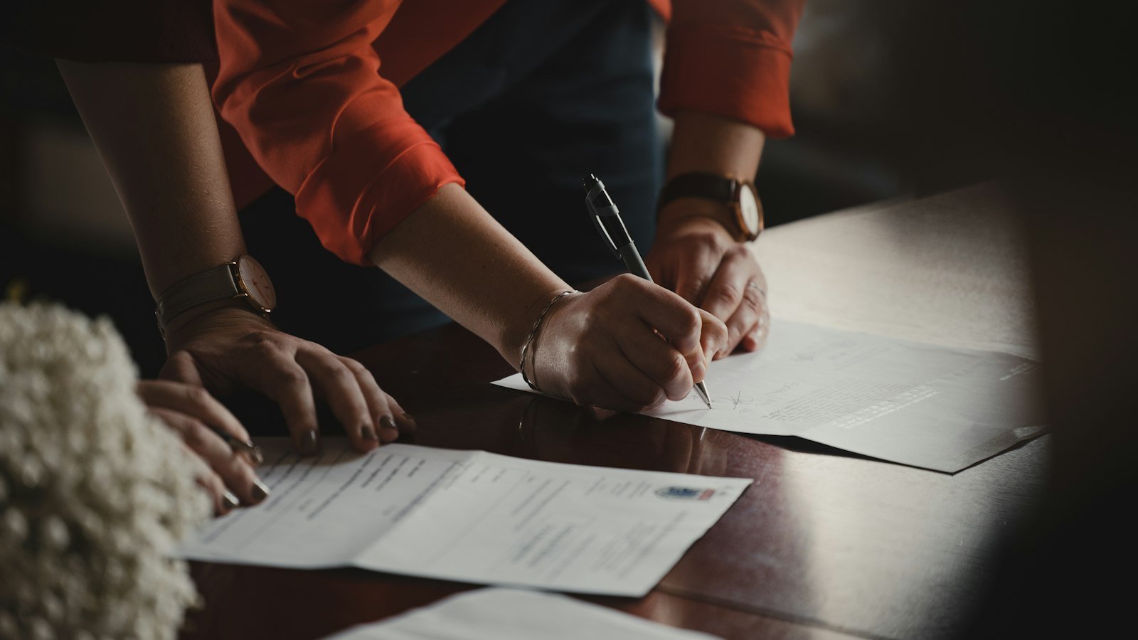 Business purchase agreement: person in orange long sleeve shirt writing on white paper