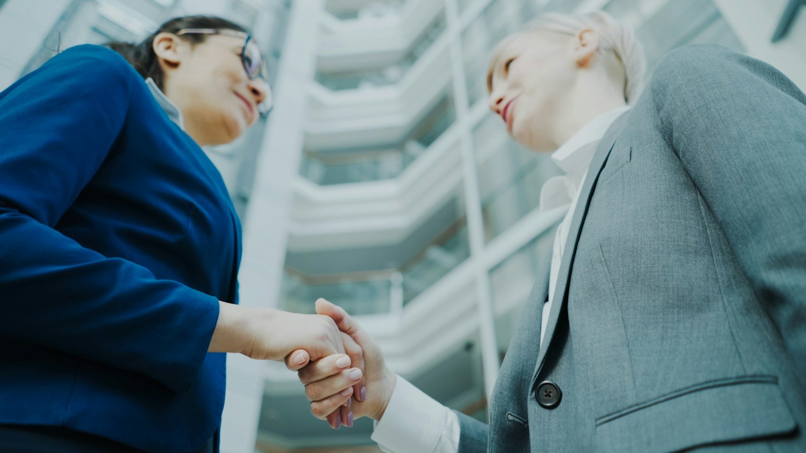 Buying and selling a business opportunity: Two businesswomen shaking hands in a modern office building
