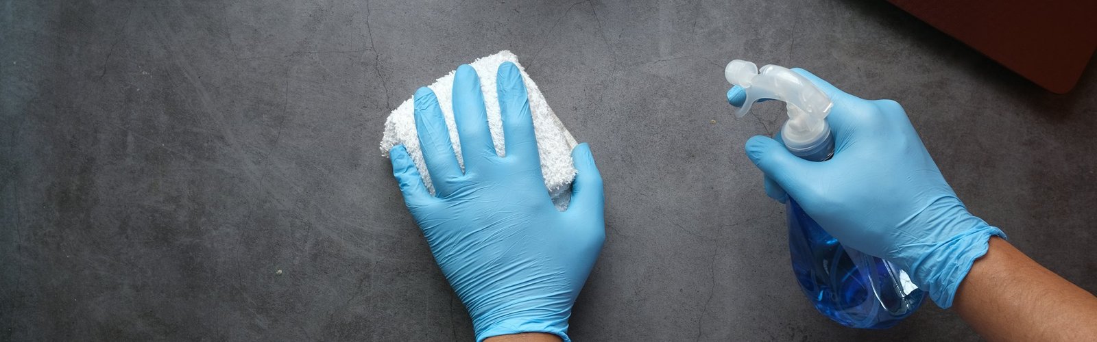 Blue-gloved hands cleaning a surface with a spray bottle
