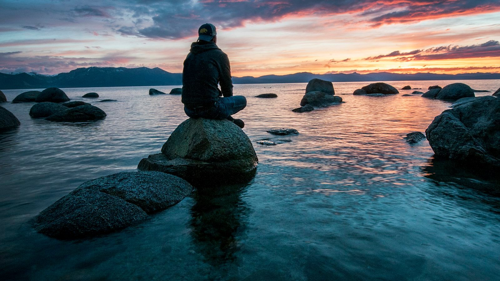 Digital detox for entrepreneurs: man sitting on rock surrounded by water