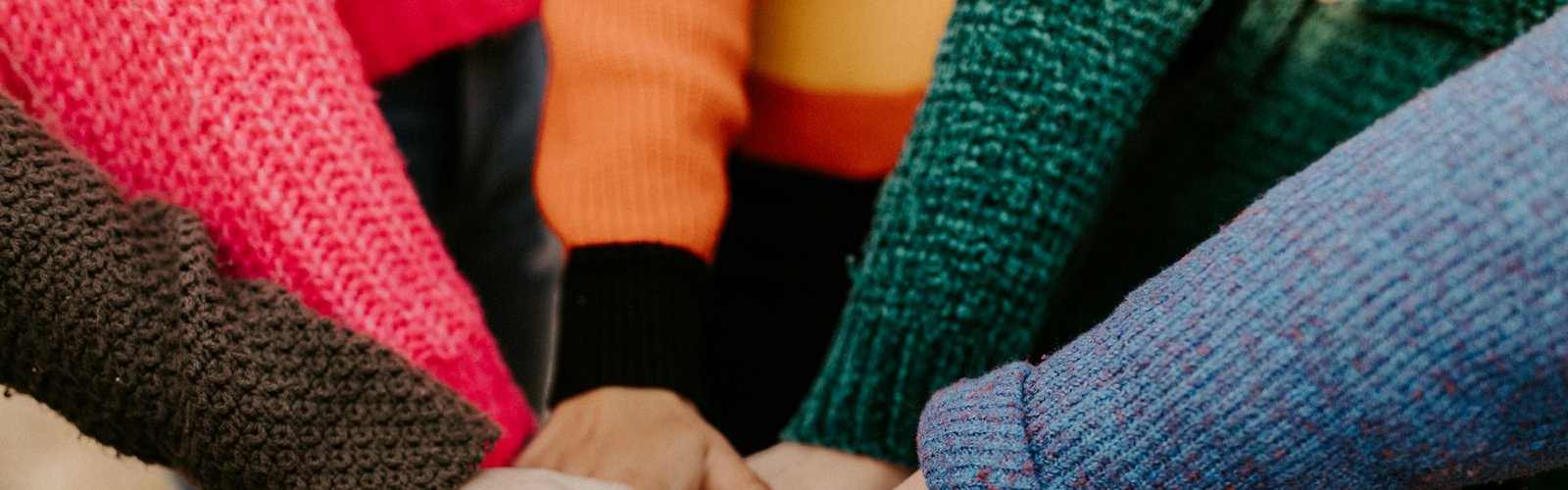 Direct sales business opportunity: Group of people stacking hands together in colorful sweaters