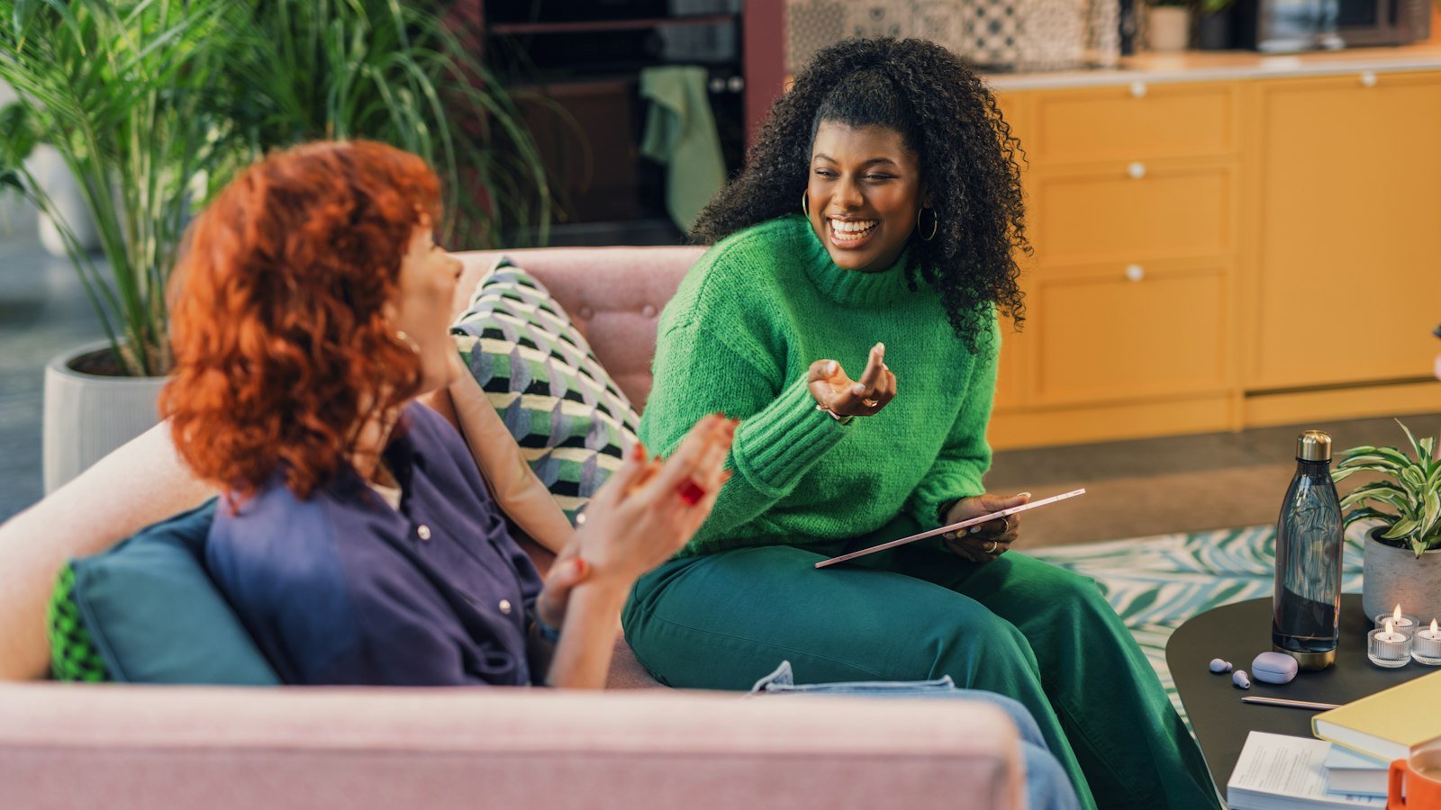 Emotional intelligence vs iq: Two women laughing while sitting on a pink sofa in a living room