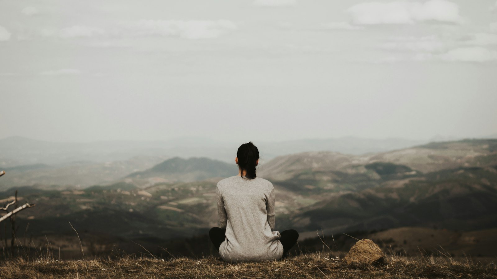 Entrepreneur wellness guide: woman sitting on cliff overlooking mountains during daytime
