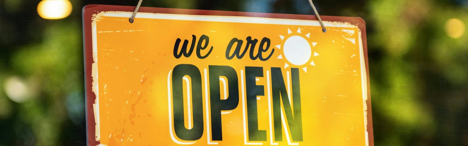 Yellow We Are Open sign hanging in a shop window
