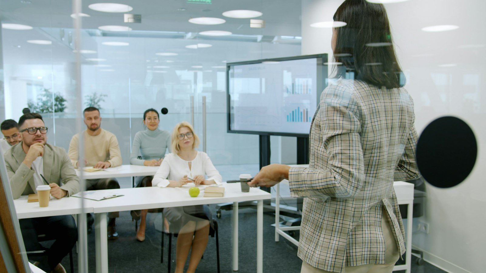 Handle sales objections: Woman presenting to an attentive audience in a modern office