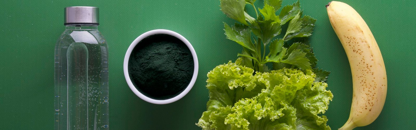 Cup of green drink beside leafy greens