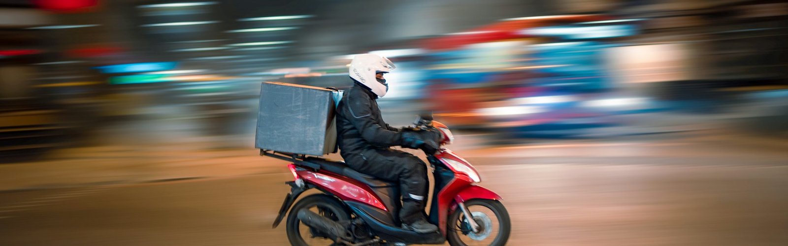 Courier on a red scooter speeding through a city street
