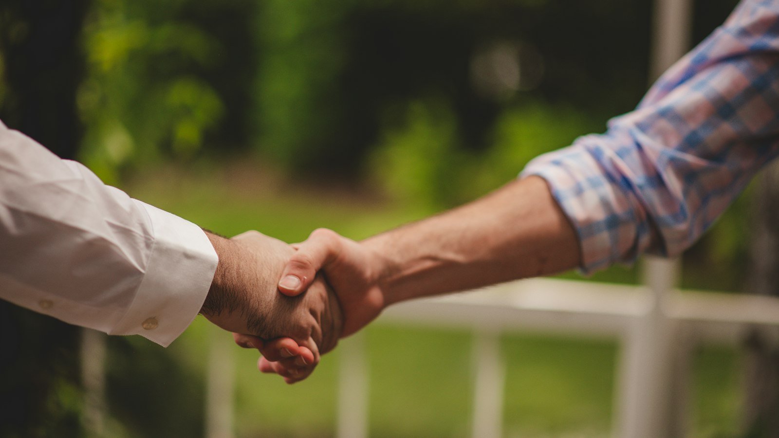Working capital adjustment: Two people shaking hands in front of a blurred green garden